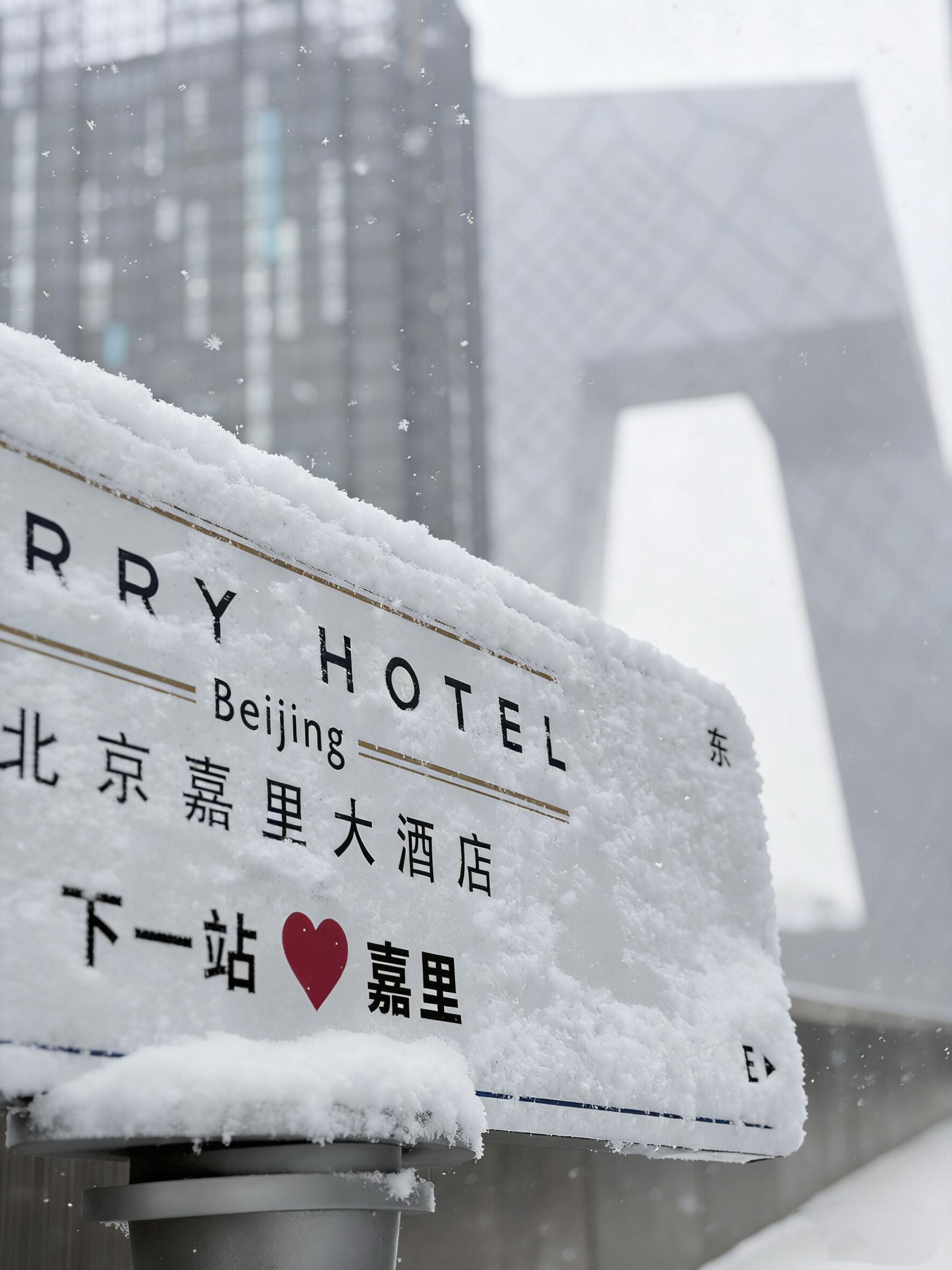 A snow-covered sign for Beijing Hotel with Chinese characters and a heart symbol indicating a location.