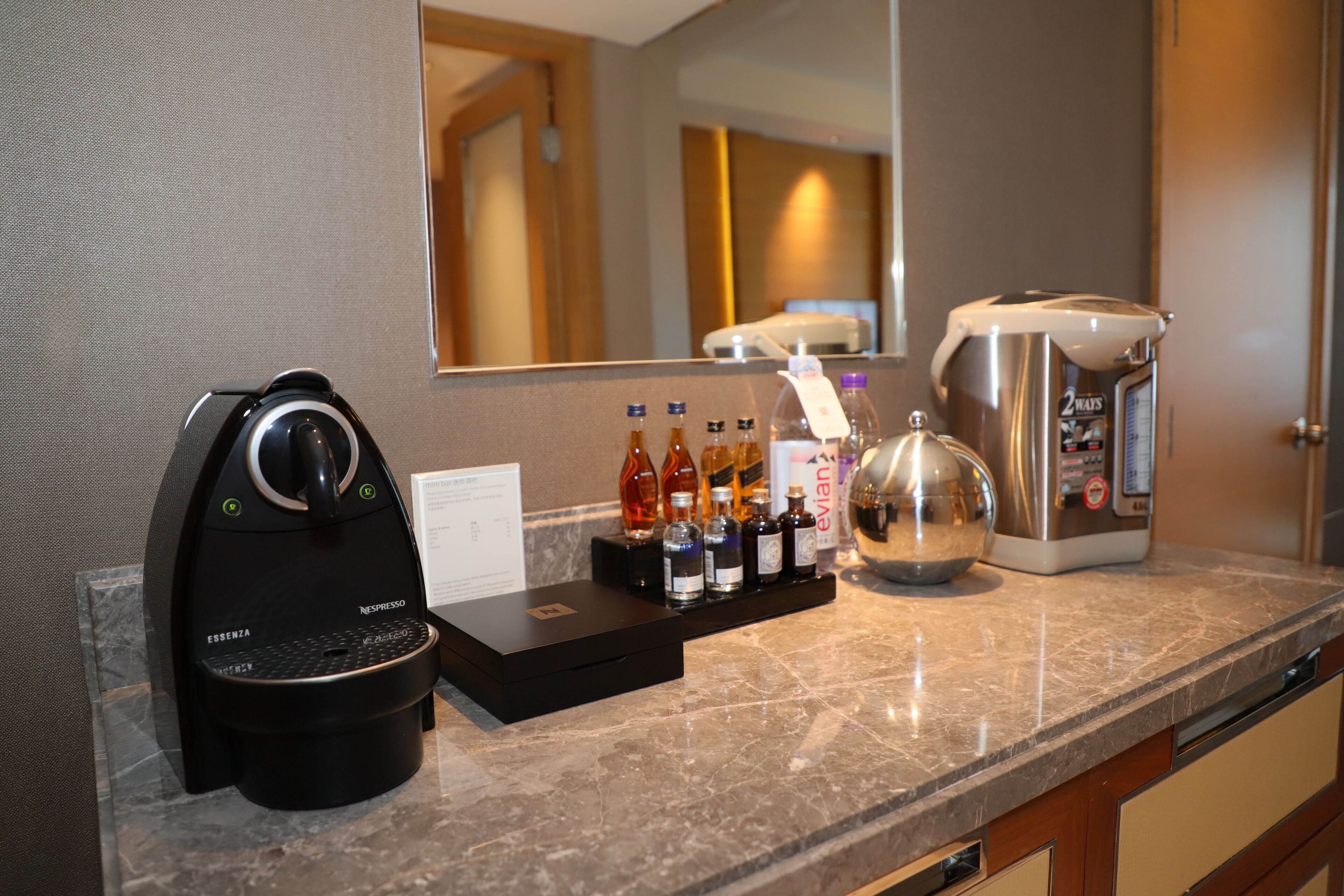 A coffee machine, a tea kettle, and a coffee maker on a marble countertop.