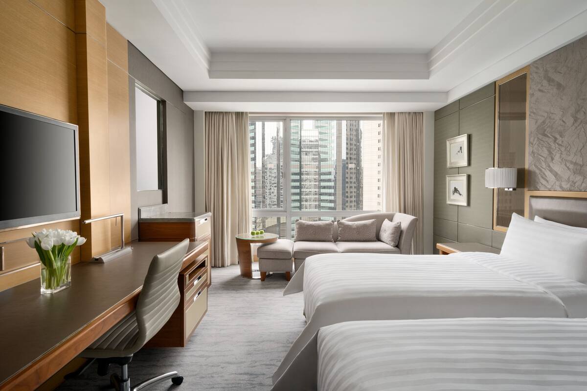 A hotel room with a large bed, a desk with a TV, a sofa, and a view of tall buildings.