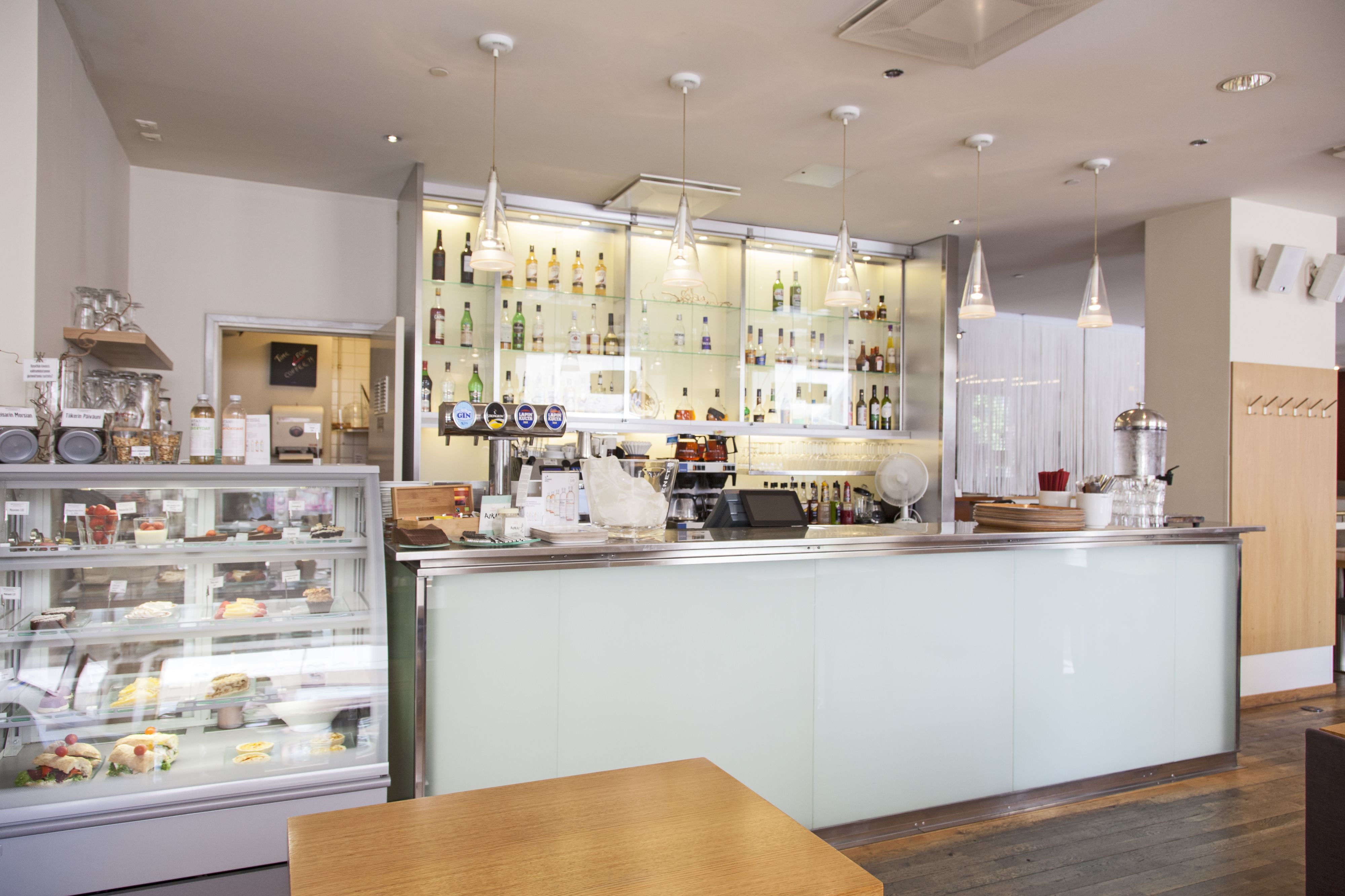 A modern cafe interior with a central counter, glass display cases, and hanging pendant lights.