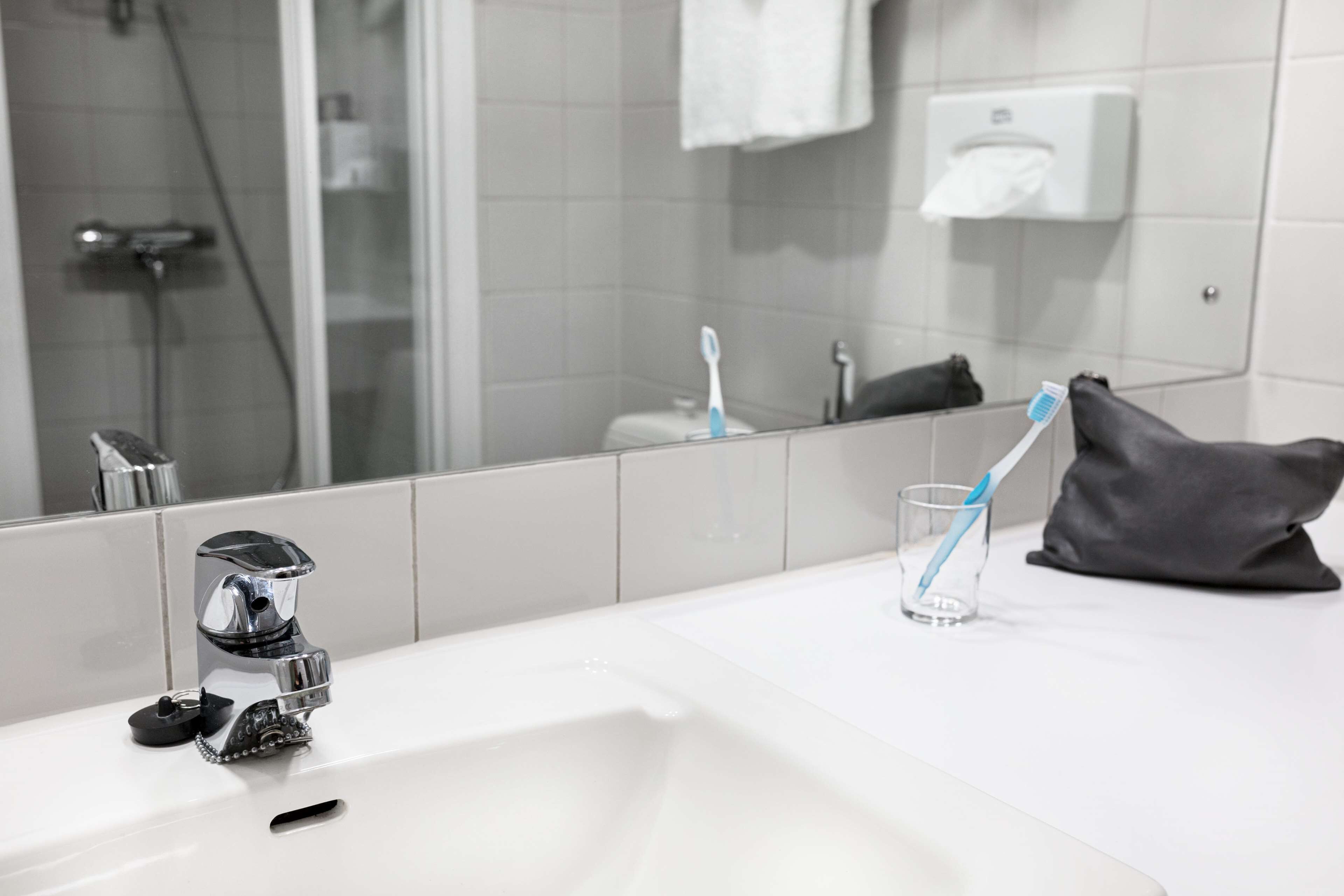 A bathroom with a white sink, chrome faucet, and a mirror reflecting a shower area.