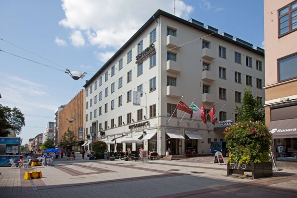 Un hotel de varios pisos con fachada moderna, zona de estar al aire libre y banderas.