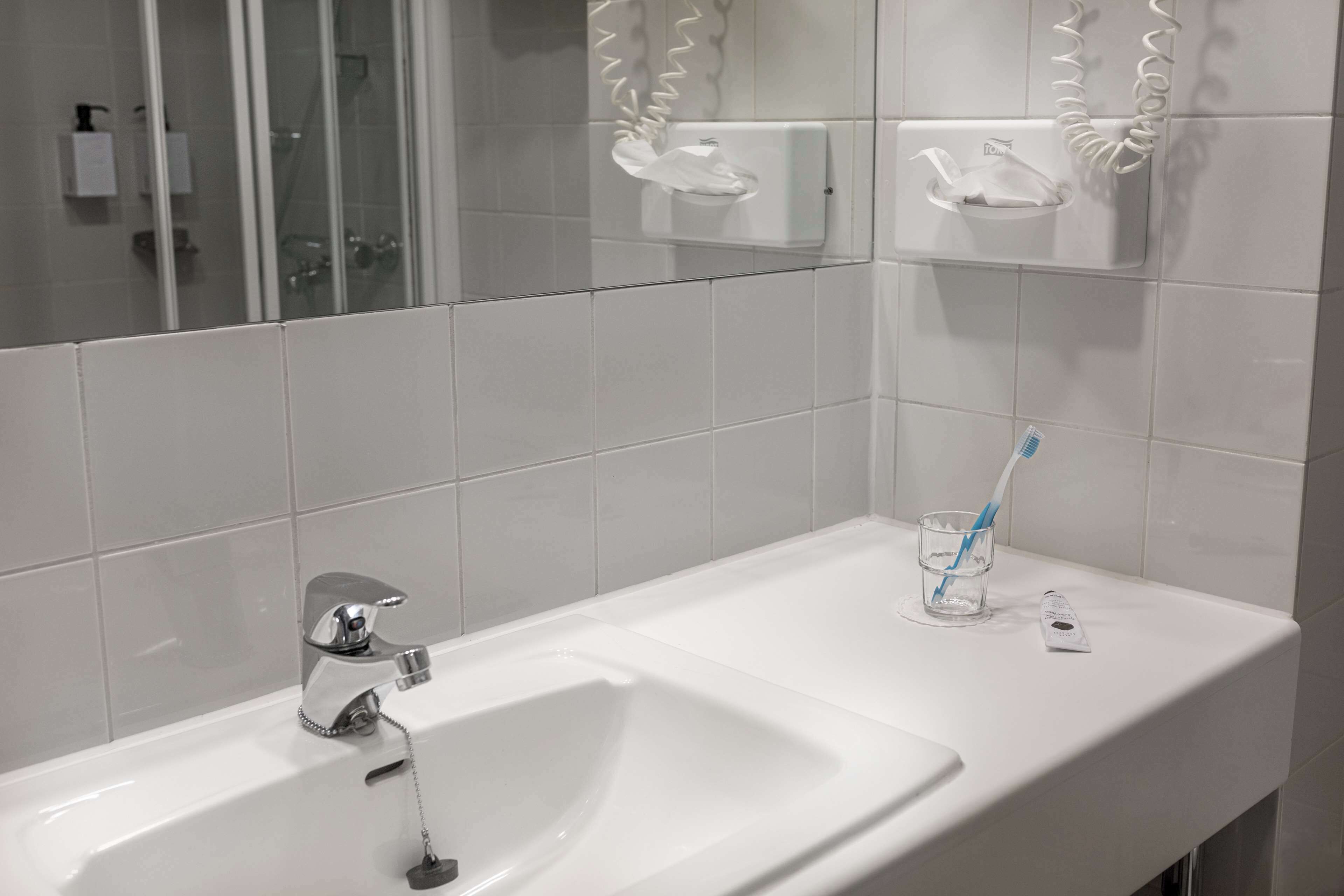 A bathroom with a white sink, a glass of water, a toothbrush, and a soap dispenser.