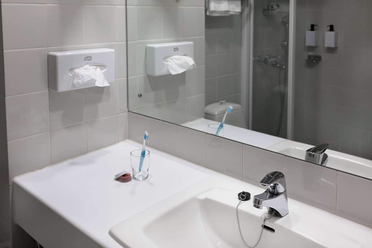 A modern bathroom with a white sink, a mirror, a glass shower enclosure, and two paper towel dispensers.