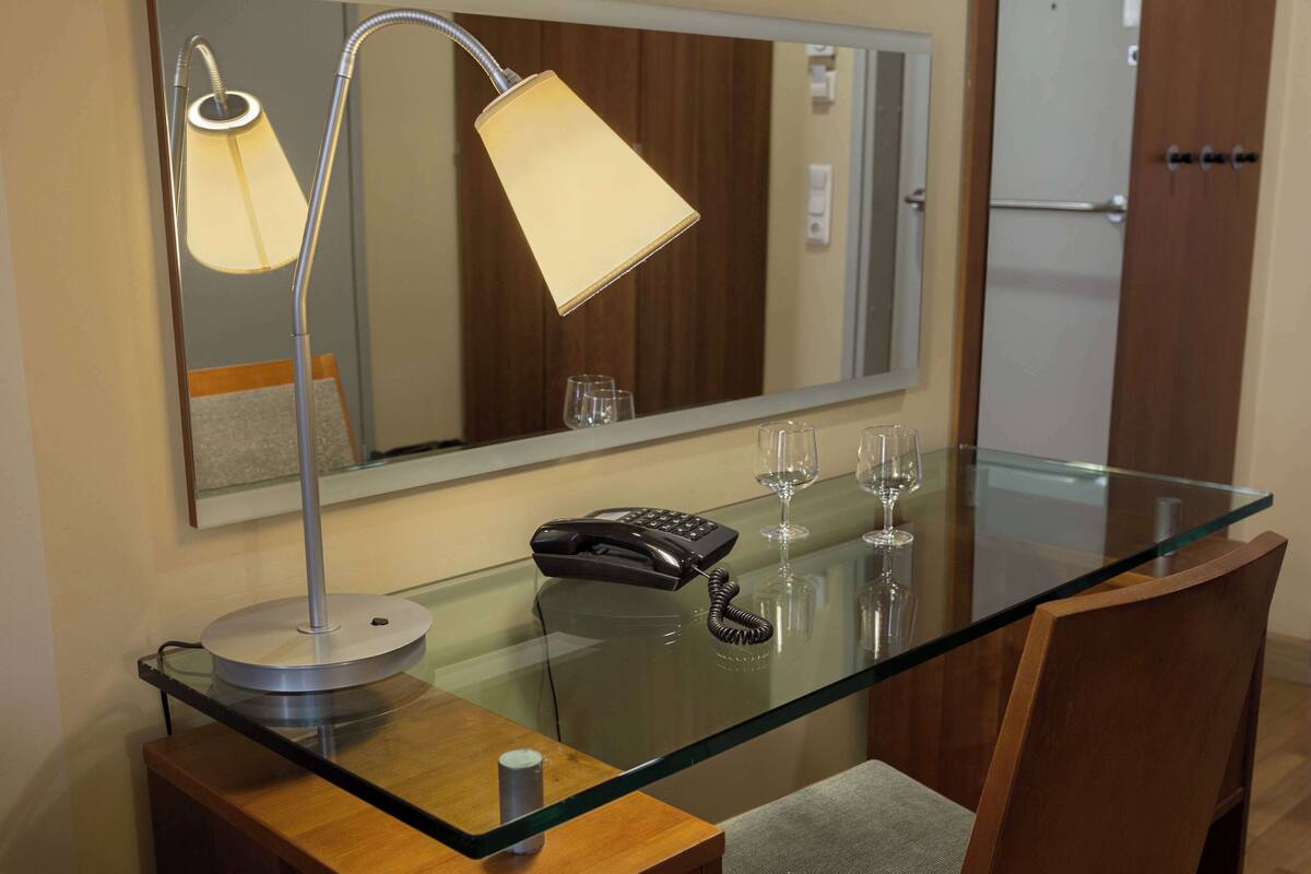 A hotel room with a glass-top desk, a telephone, and a mirror.