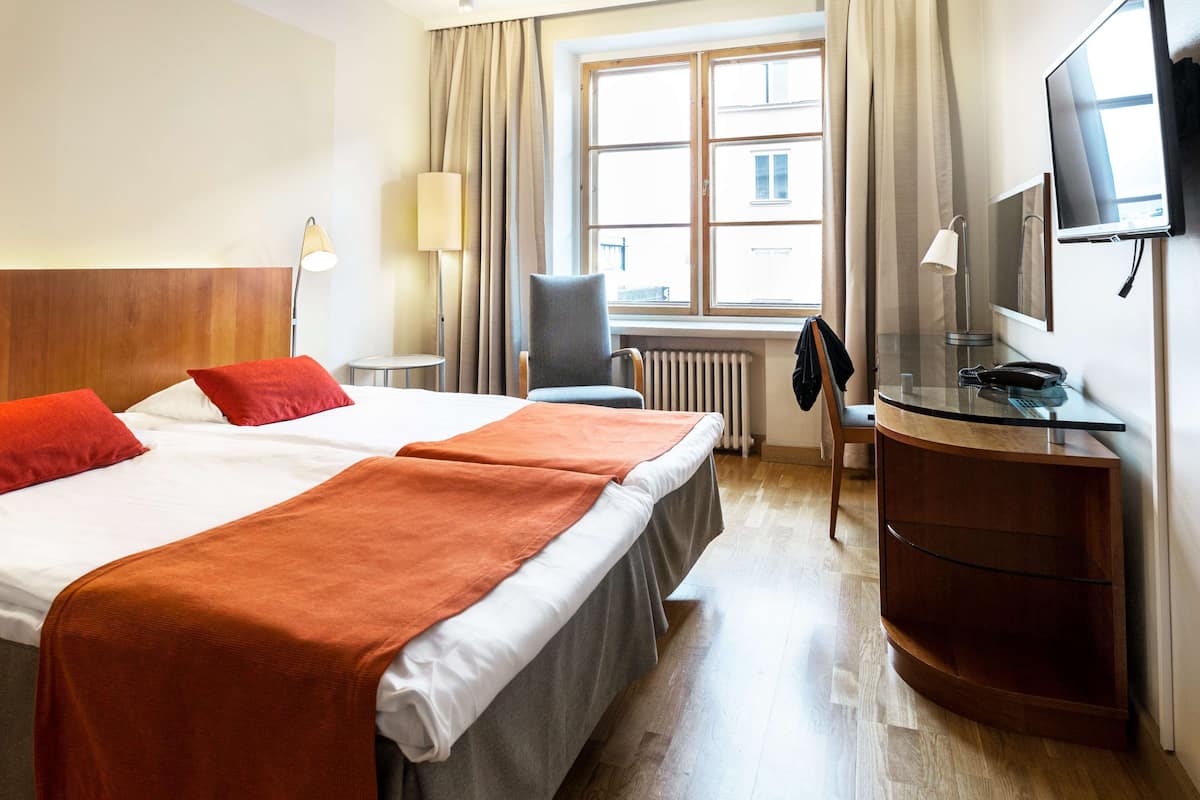 A hotel room with two beds, a desk, a chair, a TV, and a window with curtains.