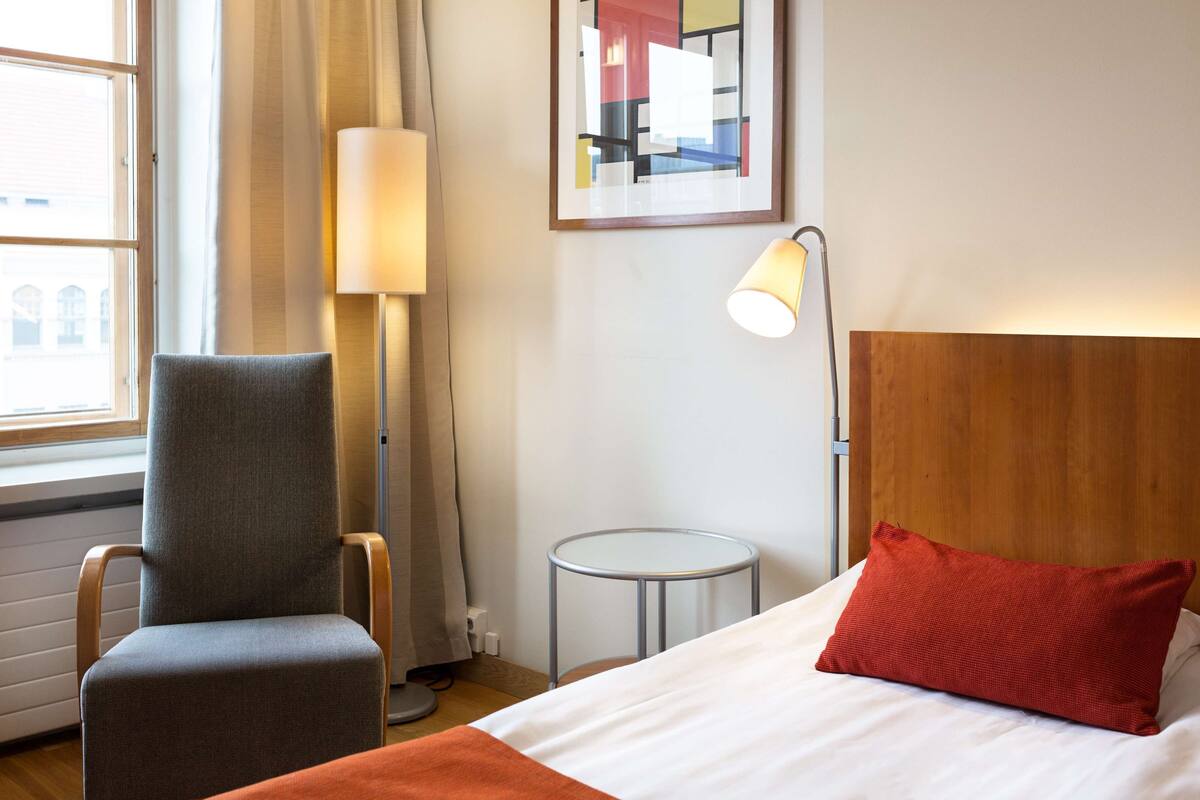 A hotel room with a bed, a chair, a lamp, and a small table.