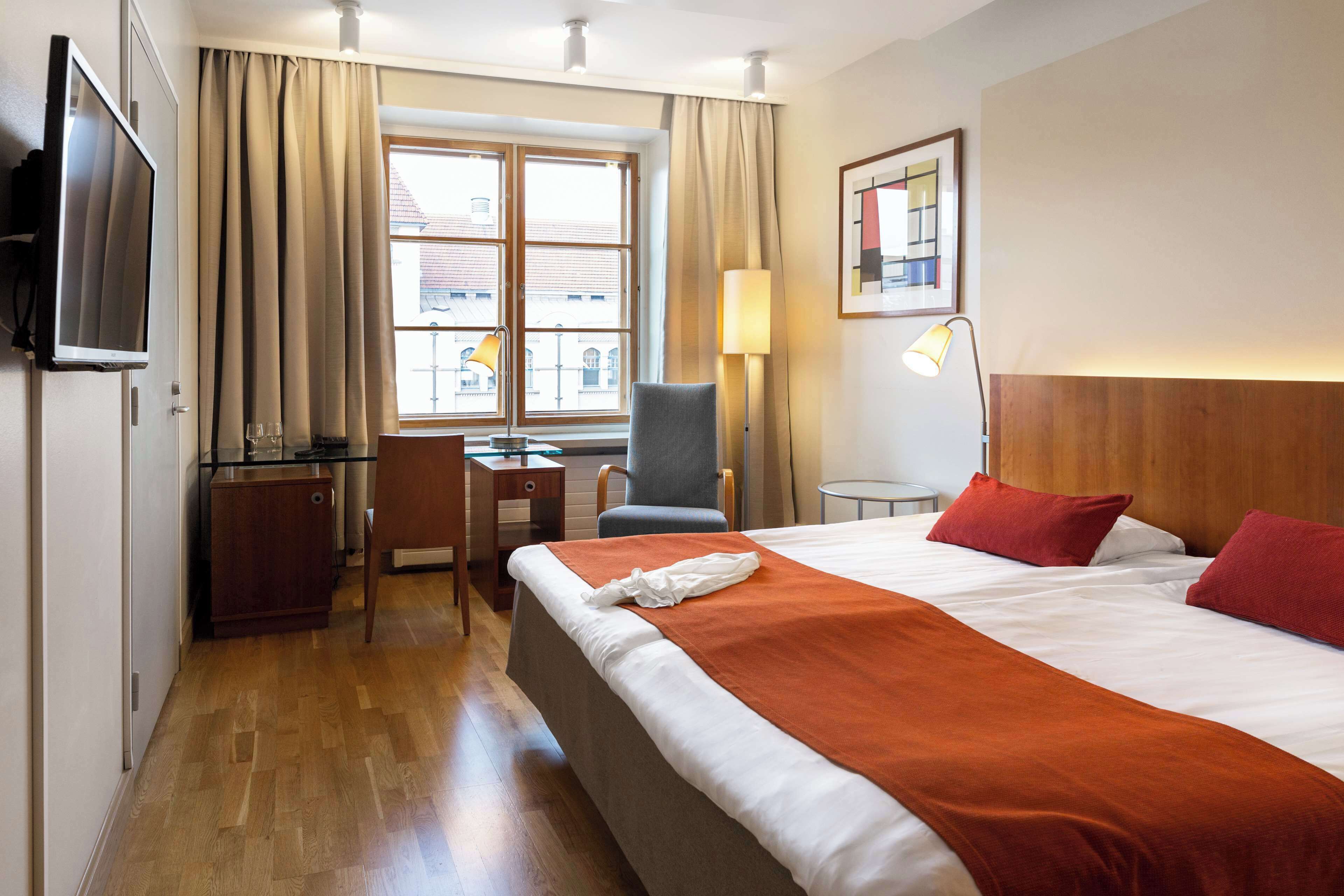 A hotel room with a bed, a desk, a chair, a TV, and a window with curtains.