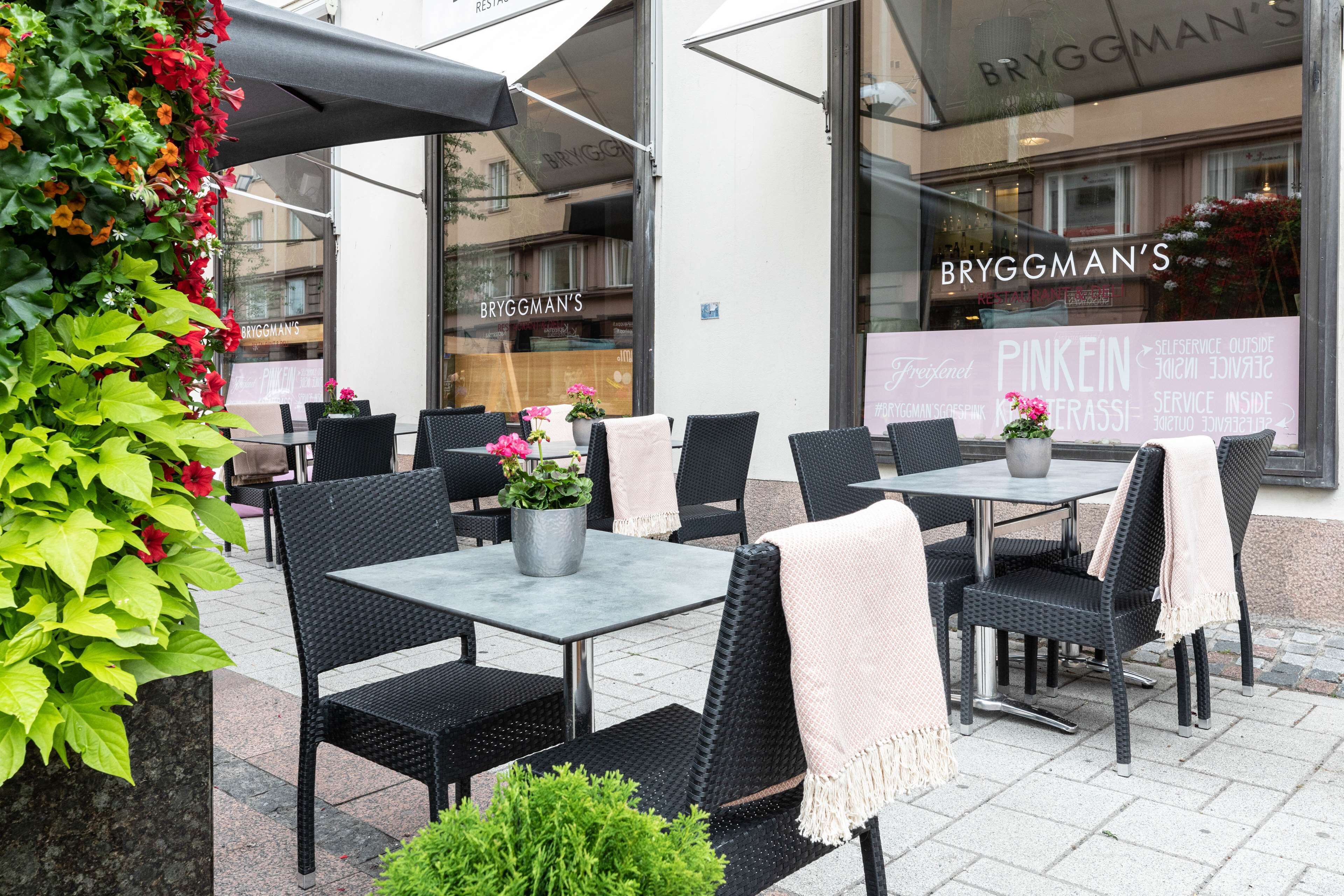 Un espace extérieur aménagé avec des tables et des chaises, des plantes en pot et une devanture de magasin avec une enseigne.