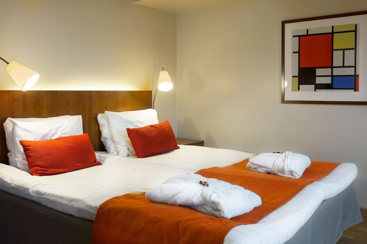 A hotel room with a bed, two pillows, a blanket, a towel, and a framed artwork on the wall.