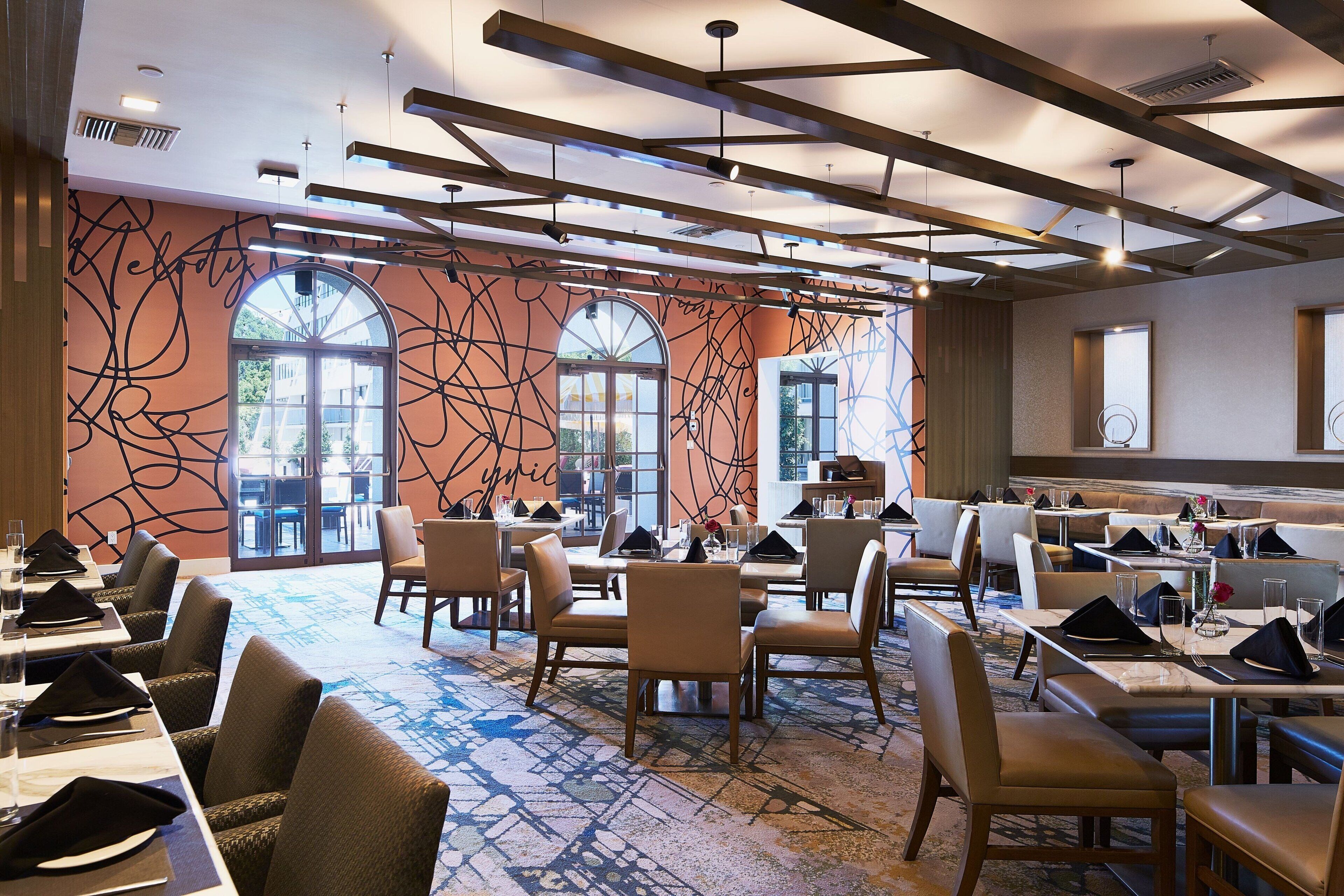 Un restaurante con una decoración moderna, que presenta una variedad de opciones de asientos, ventanas amplias y una alfombra estampada.