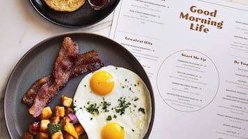 Un plato de desayuno con huevos, tocino y patatas ralladas, acompañado de tostadas y mermelada.