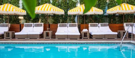 A poolside area with lounge chairs and striped umbrellas, surrounded by greenery.