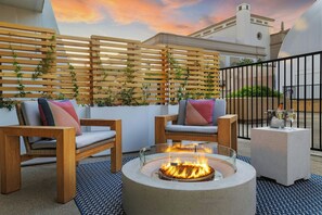 Una terraza en la azotea con un hogar para fuego, dos sillas de madera y una mesa de hormigón con vasos.