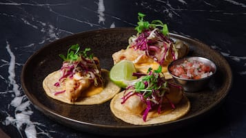 Een bord taco's met limoen en een klein schaaltje salsa op een donkere marmeren ondergrond.