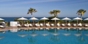 A poolside area with lounge chairs and umbrellas, overlooking the ocean.