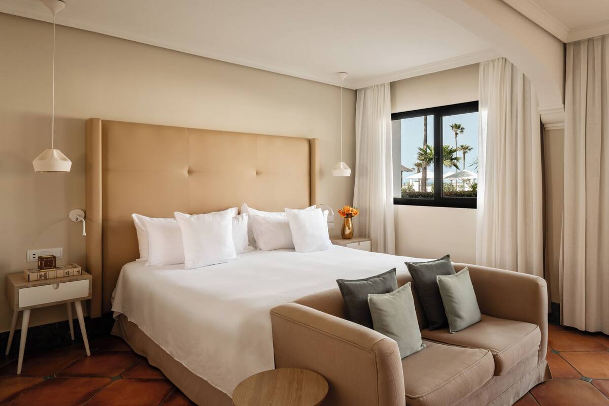 A hotel room with a large bed, a sofa, a nightstand, and a window with curtains.