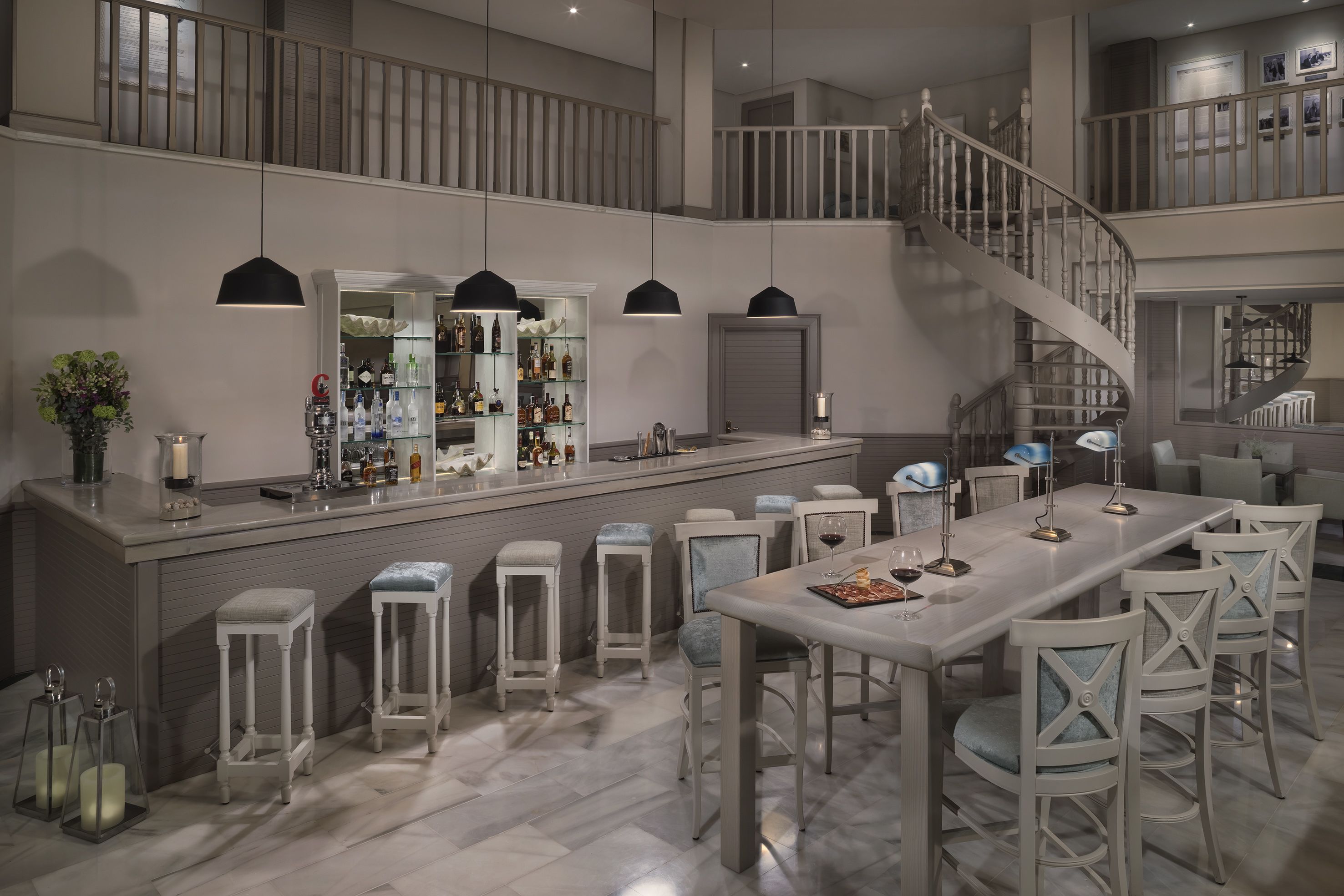 Un grand espace bar avec un plafond haut, un escalier et un coin repas comprenant de nombreuses chaises et une longue table.