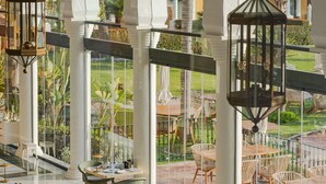 A spacious indoor dining area with multiple tables and chairs, large windows offering views of a garden, and hanging lanterns. - Palacio de Sancti Petri, a Gran Meliá - The Leading Hotels of the World (Chiclana de la Frontera)