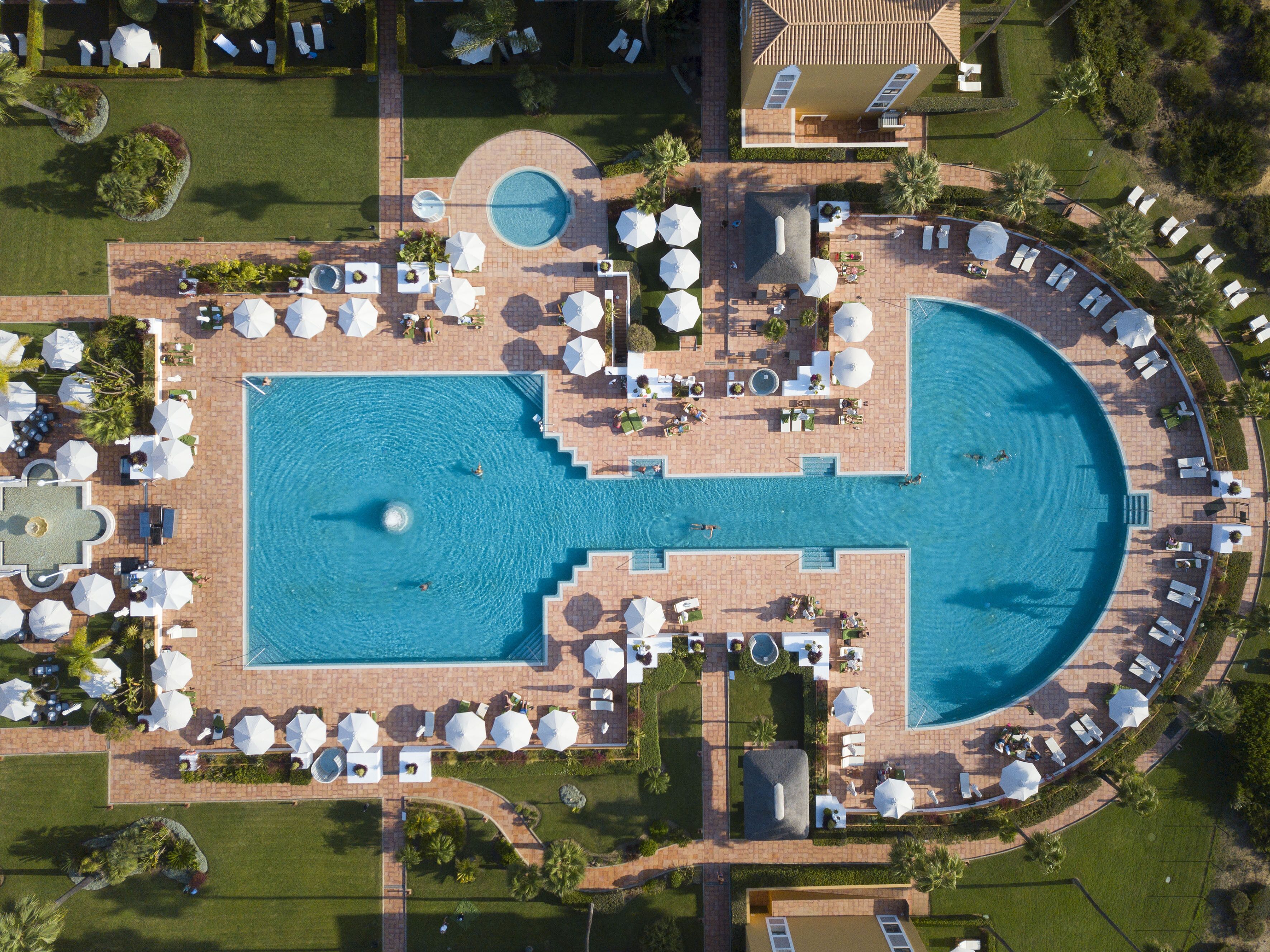An aerial view of a resort with a large central pool, multiple sun loungers, and a separate smaller pool.