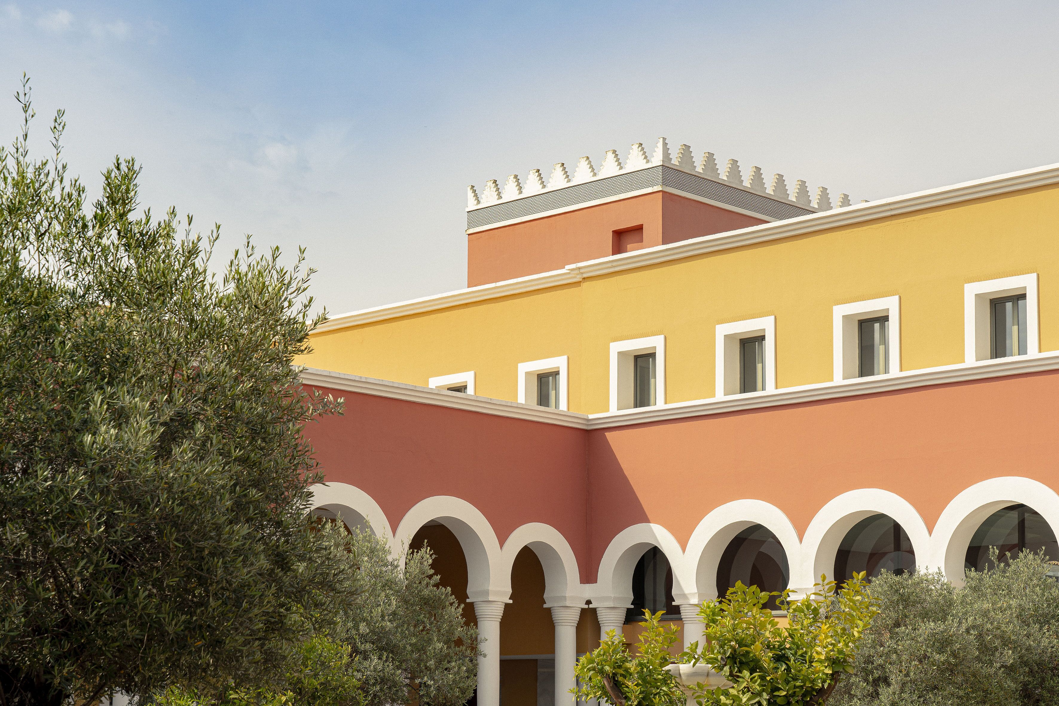 Ein Gebäude mit gelber Fassade und weißen Bögen, umgeben von viel Grün.