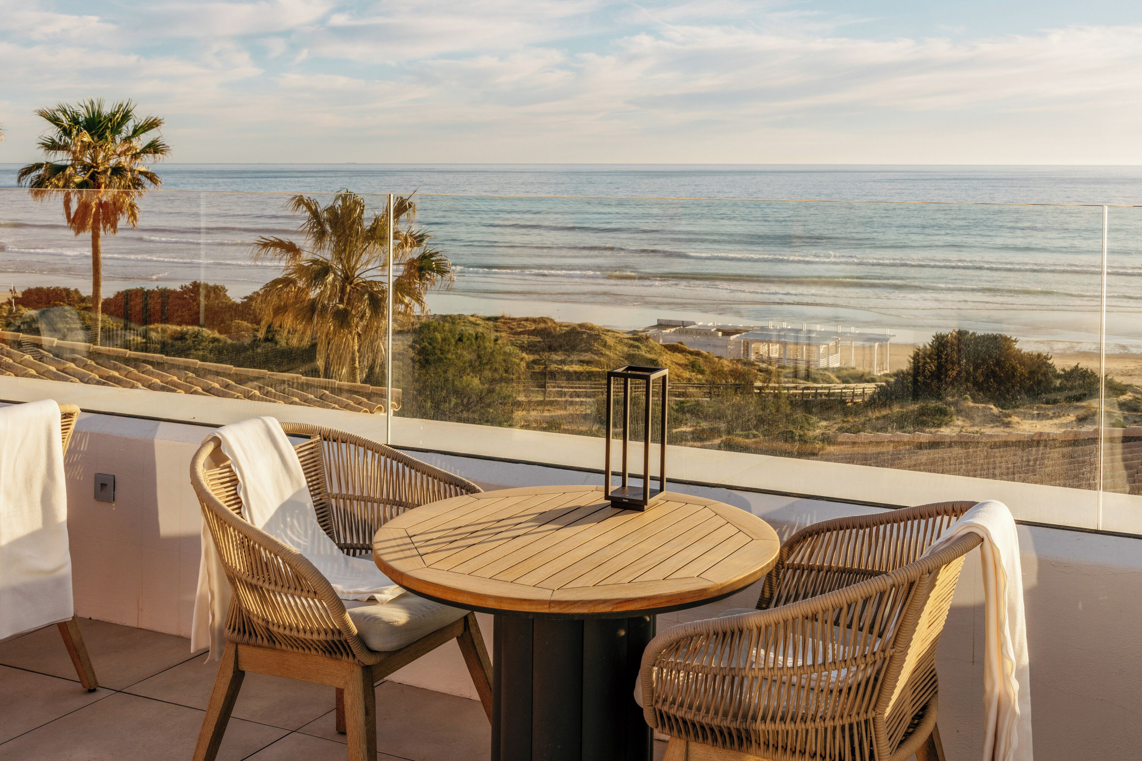 A balcony with wicker chairs and a round table, overlooking the ocean and beach.