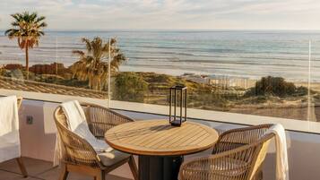 A balcony with wicker chairs and a round table, overlooking the ocean and beach.