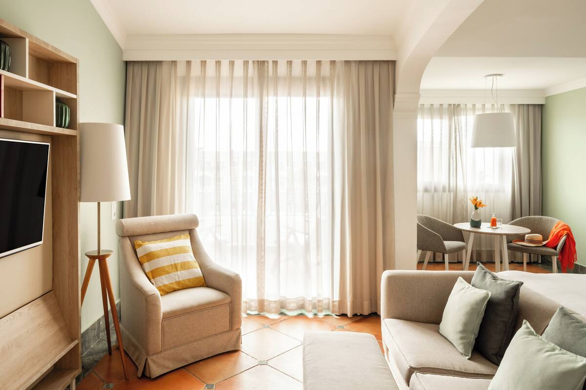 A modern living room with a sofa, armchair, and a dining area with a table and chairs.