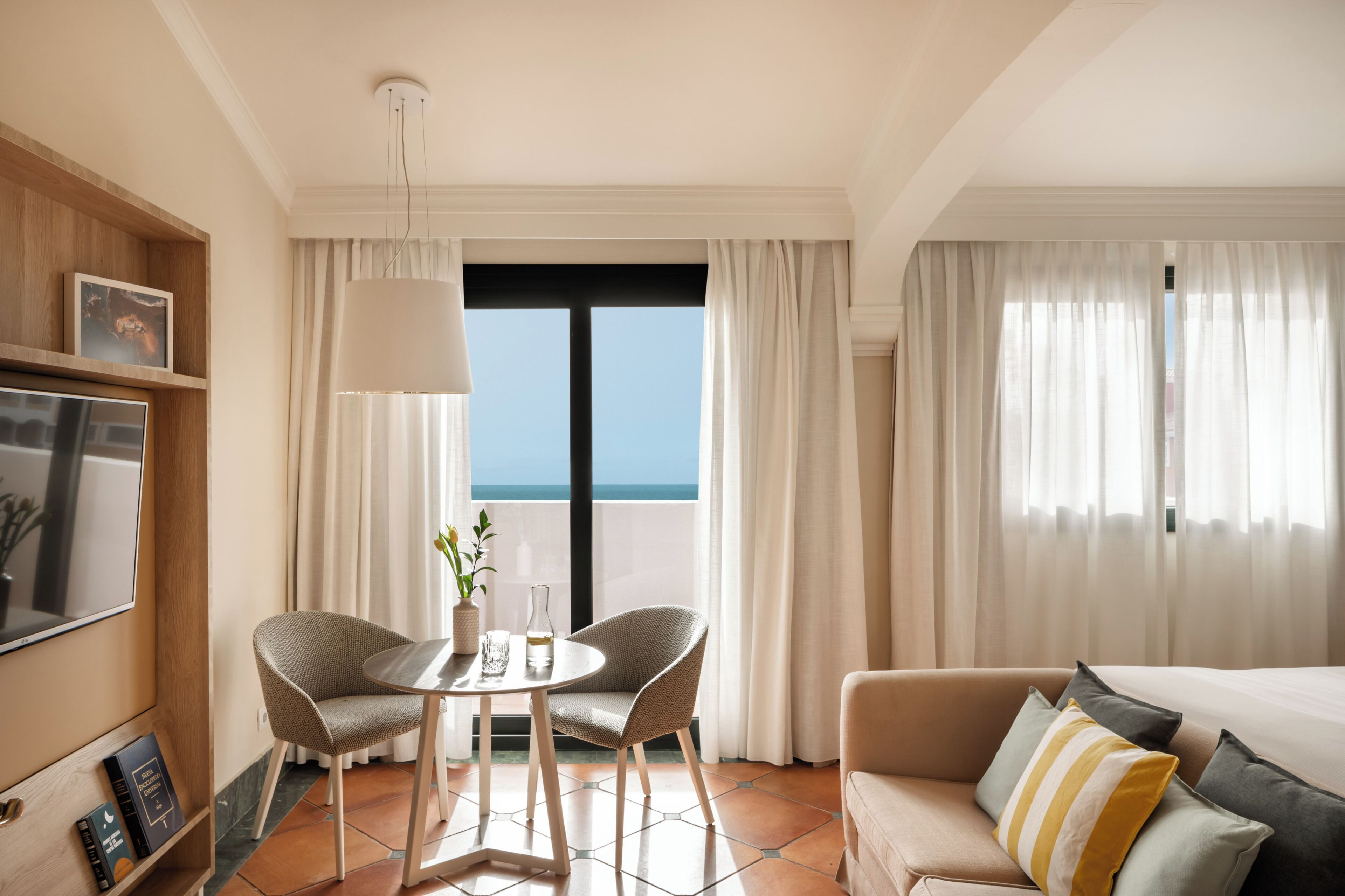 Ein Hotelzimmer mit Balkon, einer Couch, einem Esstisch mit zwei Stühlen und einem Fernseher.