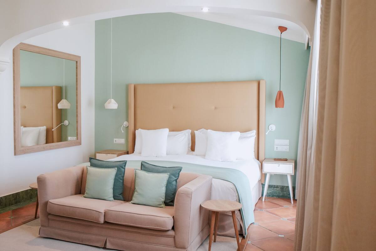 A bedroom with a bed, a sofa, a small table, and a mirror.