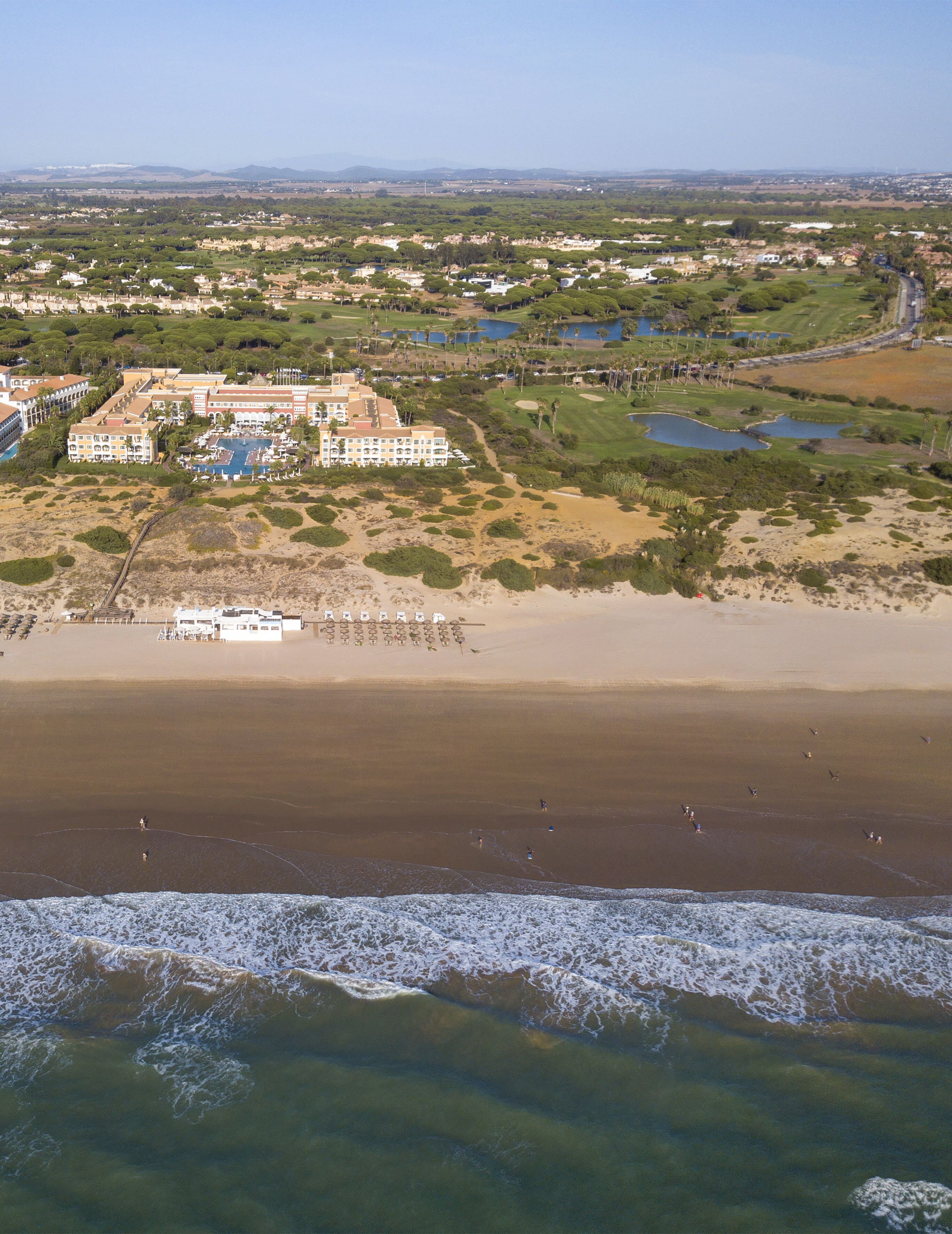 An aerial view of a coastal resort with multiple buildings, a beach, and a golf course.