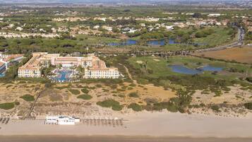 An aerial view of a coastal resort with multiple buildings, a beach, and a golf course.