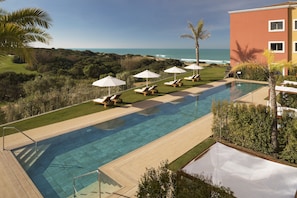 A swimming pool with lounge chairs and umbrellas, overlooking a coastal landscape.