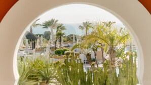 A view through a window of a resort with a pool, lounge chairs, and palm trees. - Palacio de Sancti Petri, a Gran Meliá - The Leading Hotels of the World (Chiclana de la Frontera)