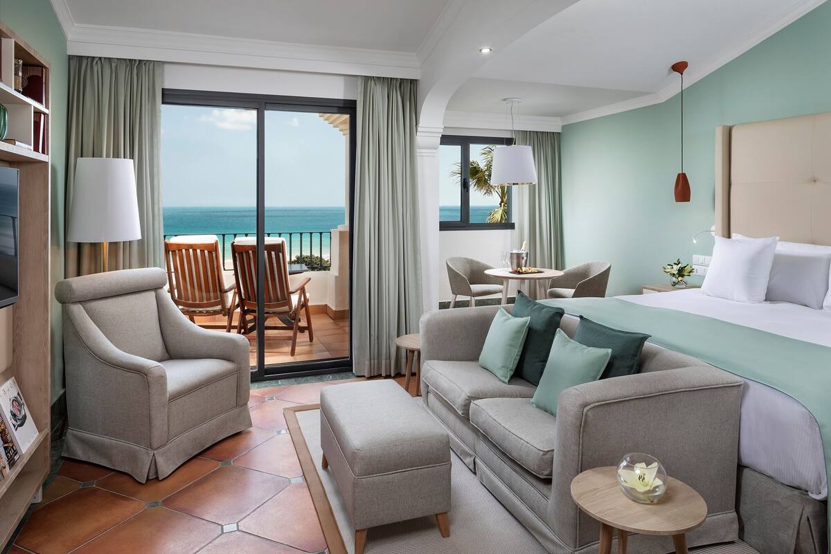 A hotel room with a balcony, a sofa, a bed, and a TV.