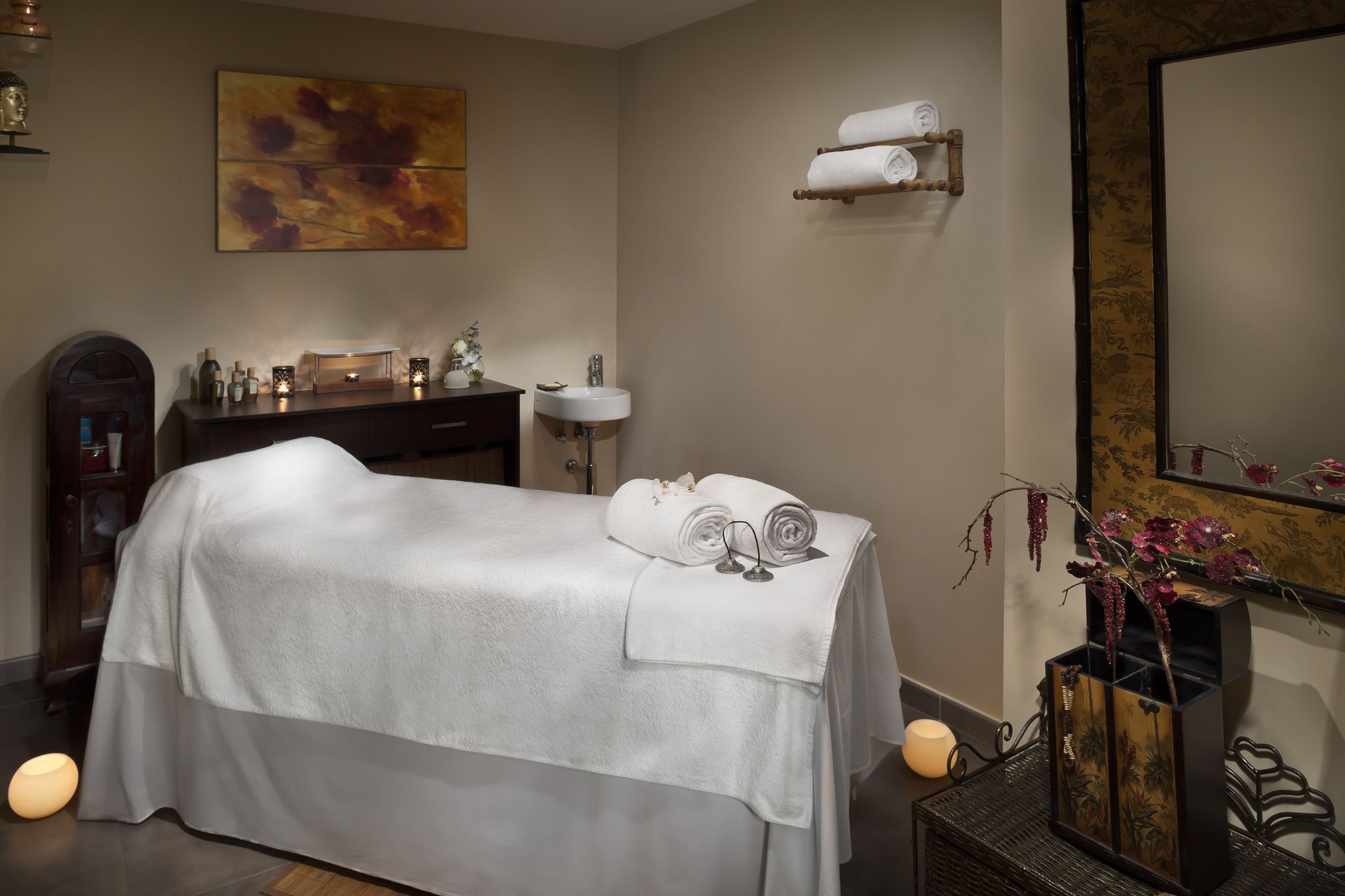 Een spa-ruimte met een massagetafel, een wastafel, een spiegel en een decoratieve vaas.