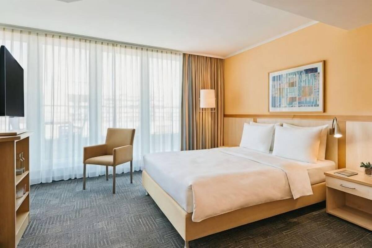 Una habitación de hotel con cama, una silla, un escritorio, una lámpara y un cuadro en la pared.