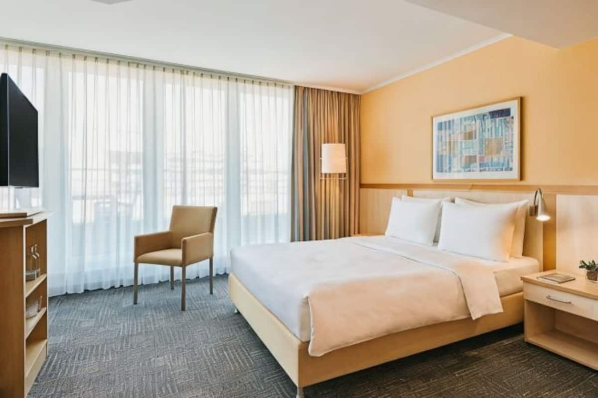 Una habitación de hotel con cama, una silla, un escritorio, una lámpara y un cuadro en la pared.
