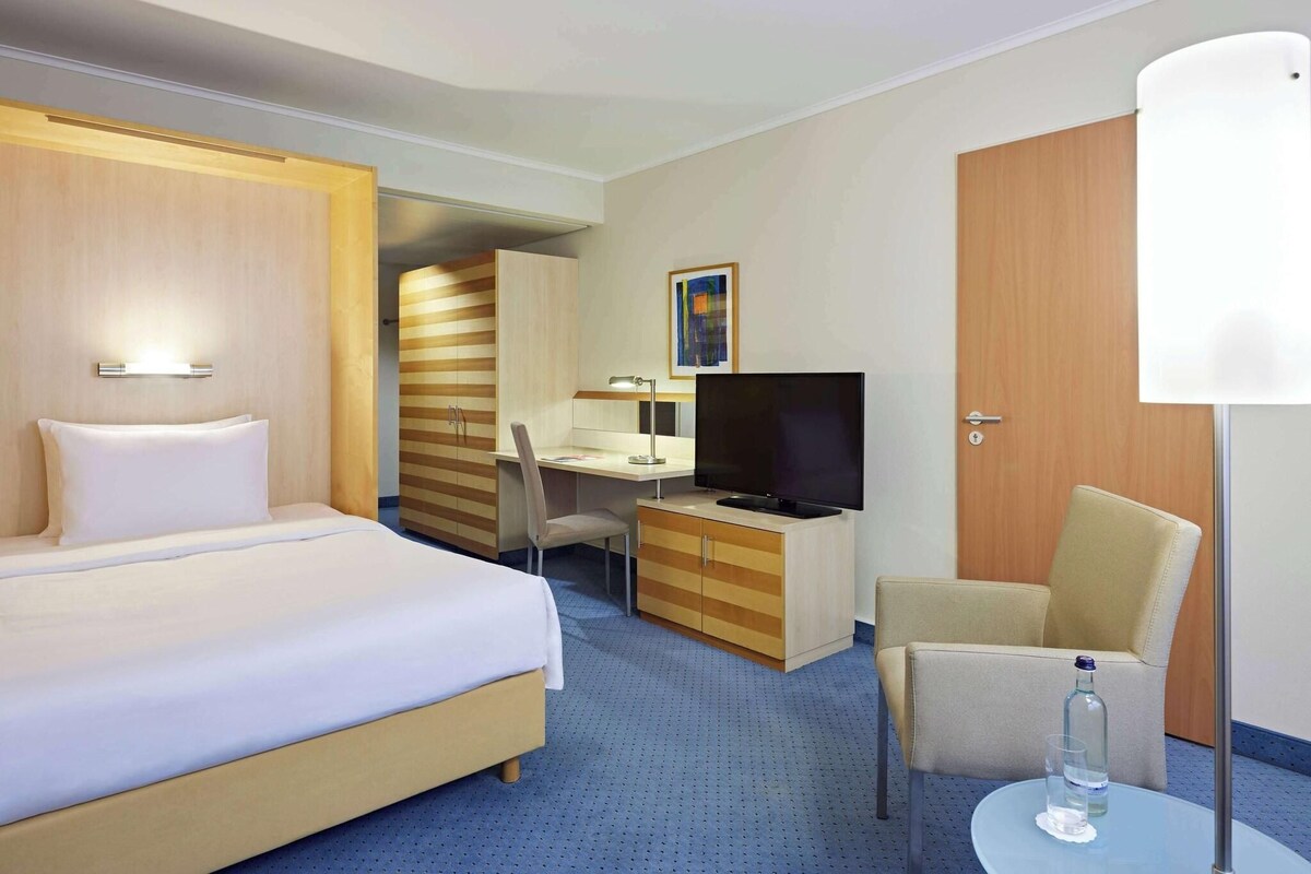 A hotel room with a bed, a desk, a chair, a television, and a lamp.