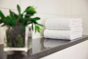 A stack of white towels on a reflective countertop with a potted plant in the background.