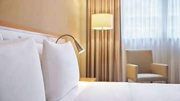 Habitación de hotel con una cama bien hecha, una lámpara, una silla y vistas a cortinas y un ventanal.
