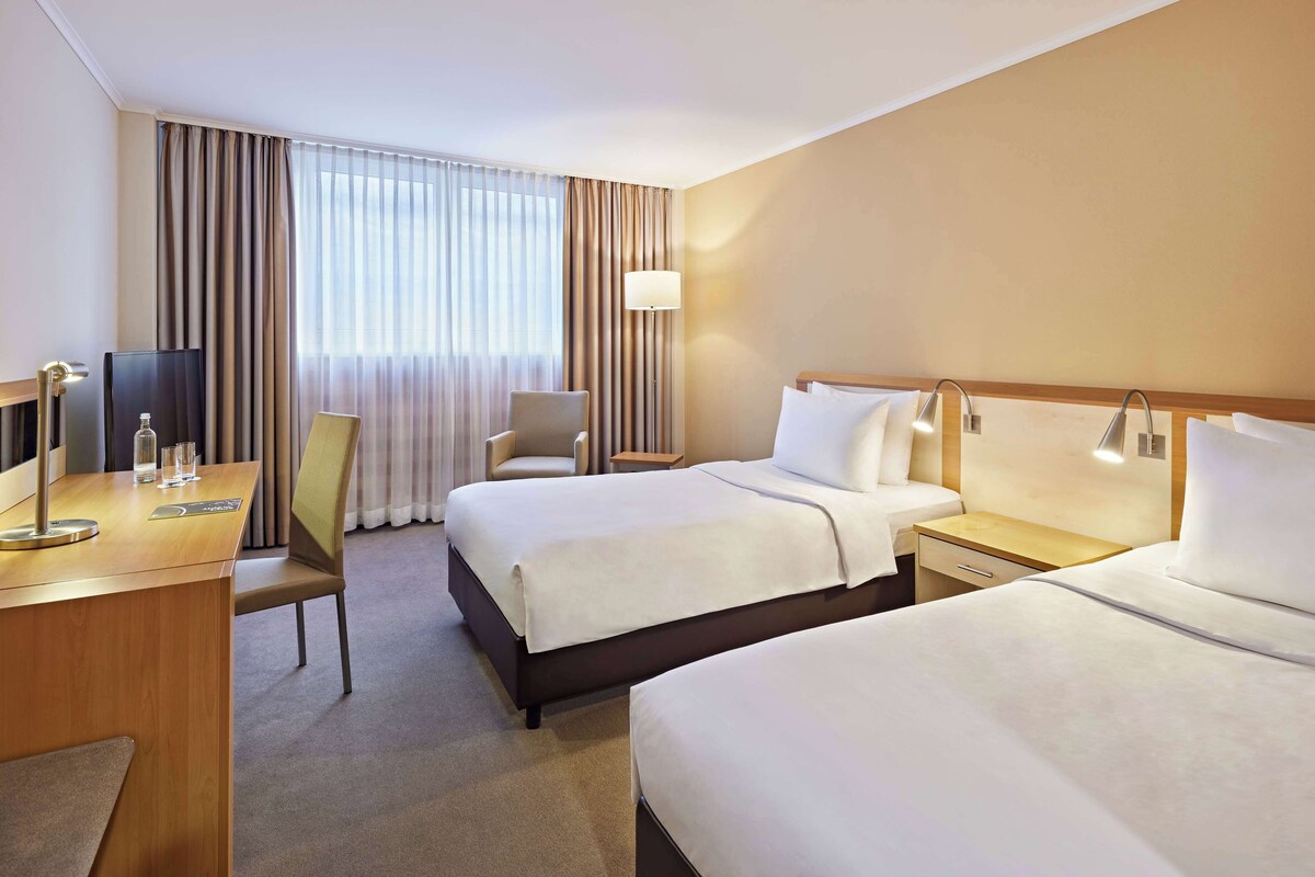 Une chambre d’hôtel avec deux lits, un bureau, une chaise, une télévision et une lampe.