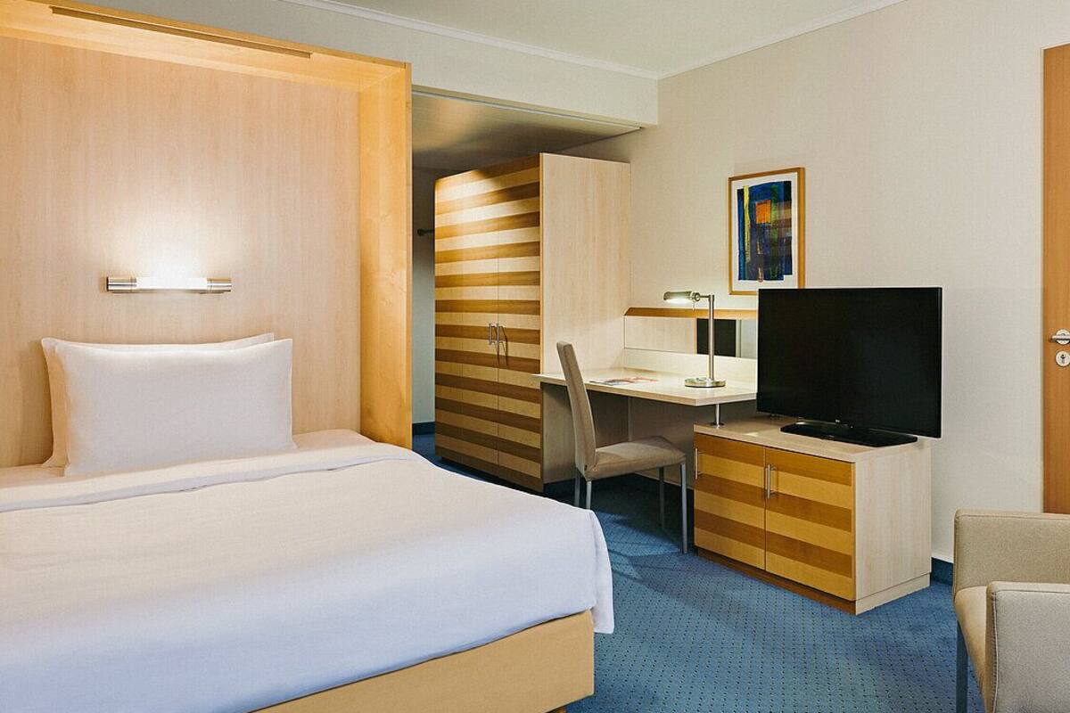 Una habitación de hotel con cama, escritorio con televisor, silla y armario.