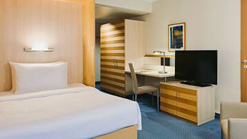 A hotel room with a bed, a desk with a television, a chair, and a wardrobe.