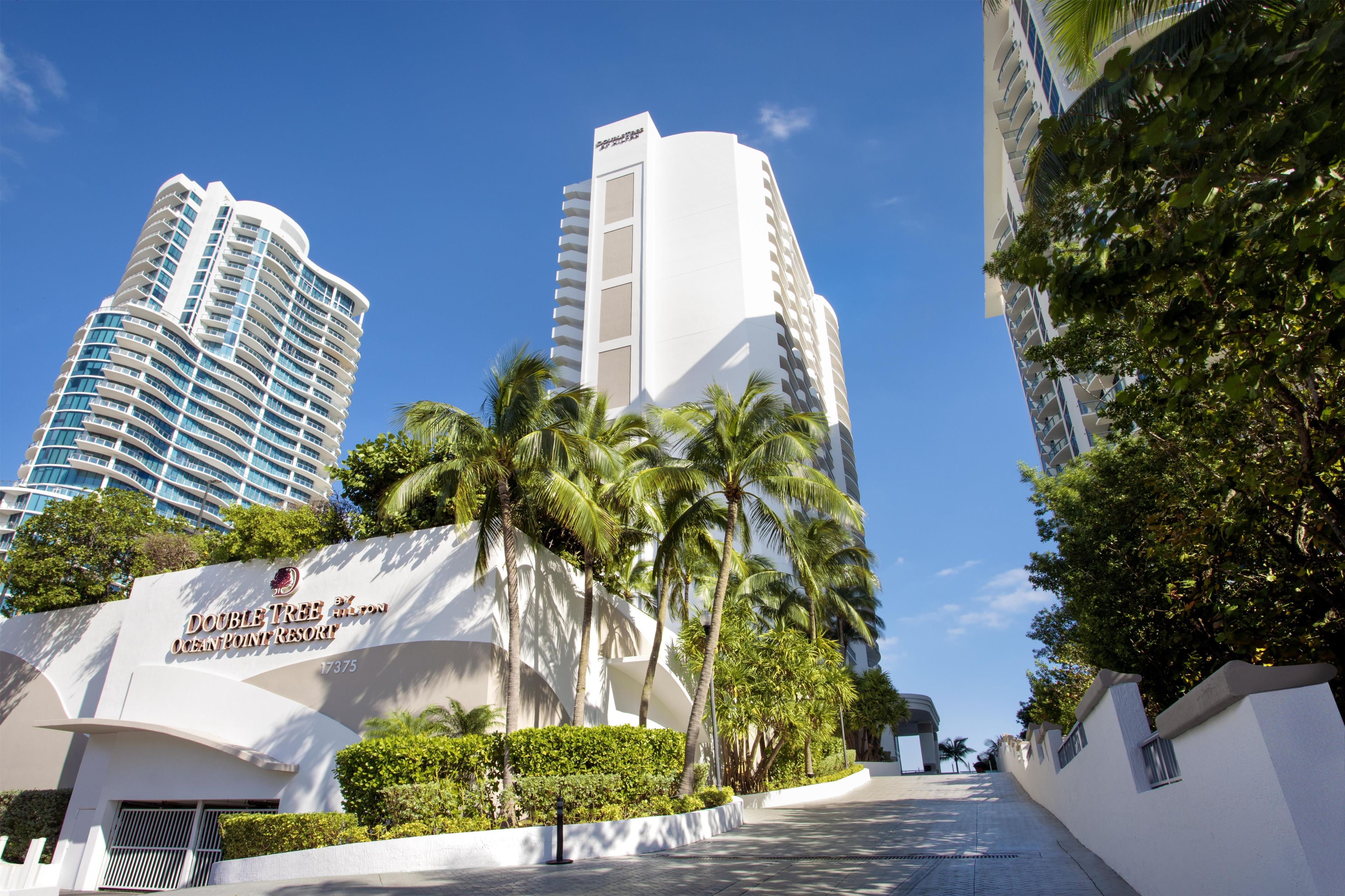 A modern hotel with a curved facade, palm trees, and a clear blue sky.