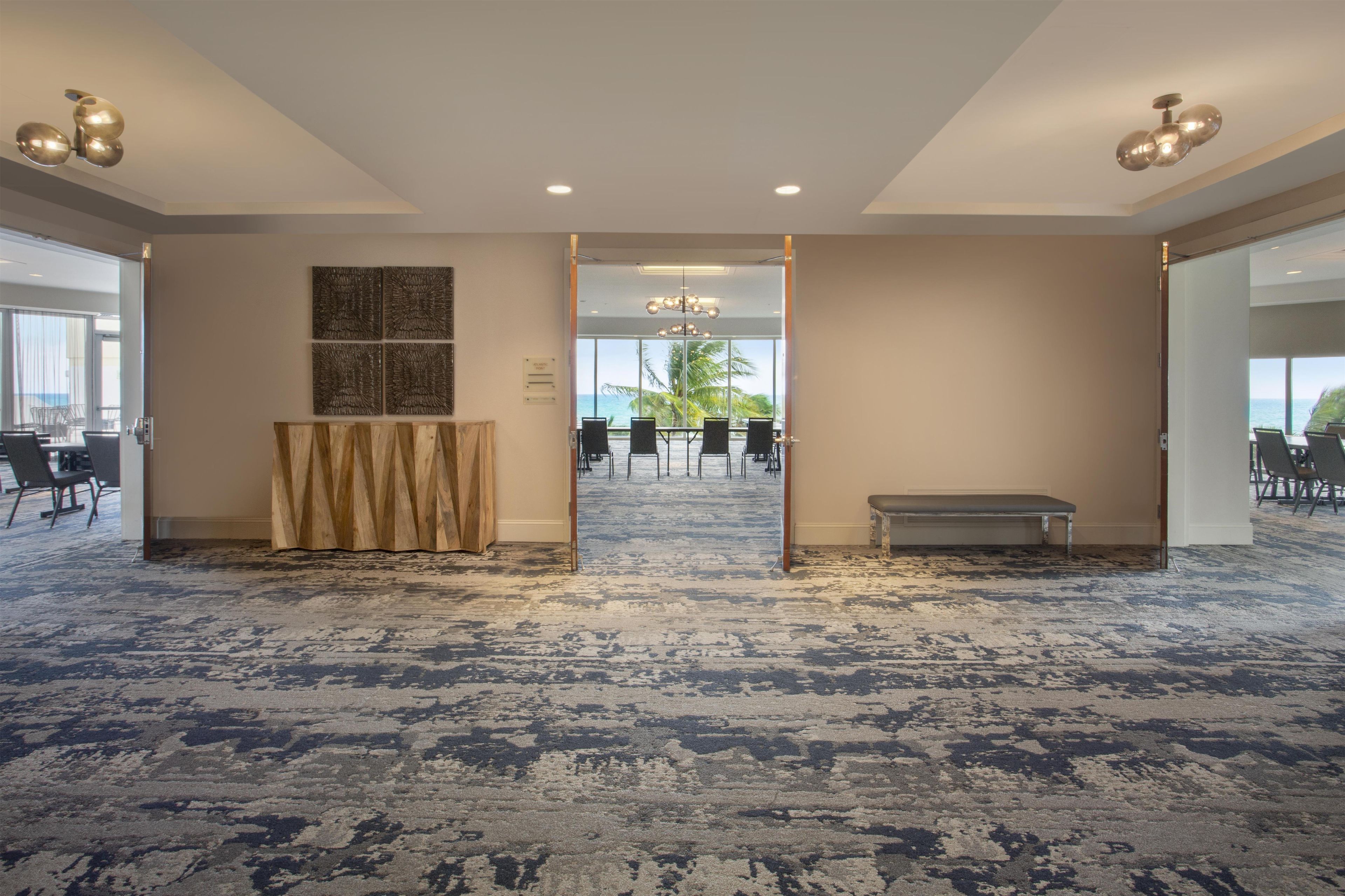A spacious hotel lobby with a patterned carpet, a reception desk, and a view of the outdoors.