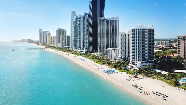 A coastal cityscape with high-rise buildings, a beach, and a pier.