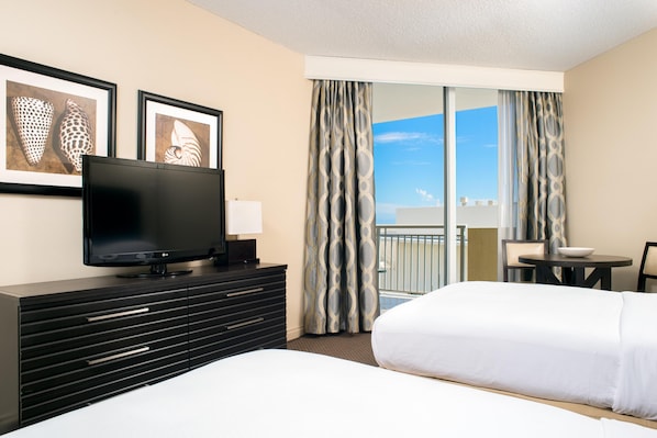 Une chambre d’hôtel équipée d’une télévision à écran plat, d’un lit, d’une commode, d’un bureau avec une chaise et d’un balcon avec des rideaux.