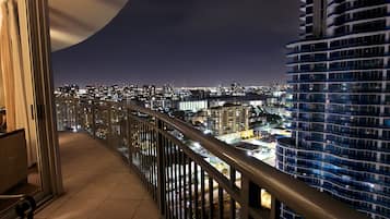 A balcony with a view of a cityscape at night, featuring high-rise buildings and a river.