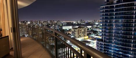 A balcony with a view of a cityscape at night, featuring high-rise buildings and a river.